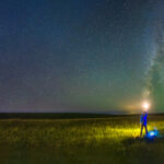 The man holds the lamp on the grassland under the Milky Way