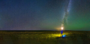 The man holds the lamp on the grassland under the Milky Way
