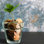 clear glass filled with pennies with a plant sprouting out of it